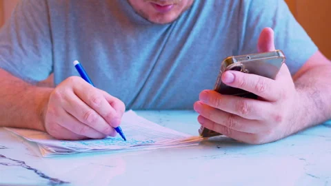 Close up shot of using a cellphone screen to cross-reference data on paperwork Stock Footage 336692412