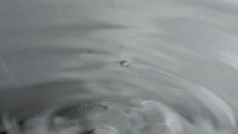Close up shot of water drop falling into liquid surface creating circular Stock Footage 343968799