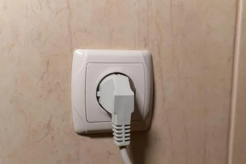 A close-up shot of a white electrical plug inserted into a wall socket Stock Photos