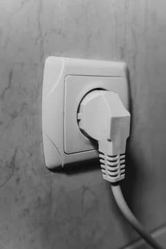 A close-up shot of a white electrical plug inserted into a wall socket Stock Photos