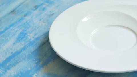 Close up shot of a white plate rotating on a blue table. Video stock 105738294