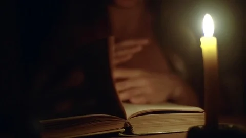 Close-up shot of a woman reading a book in dark room under light of a candle. Stock Footage