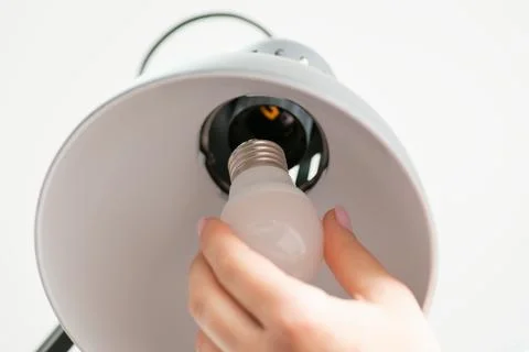 Close up shot of woman's hand changes a light bulb in grey lamp Stock Photos
