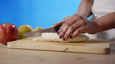 Close-up shot of a woman's hands slicing a banana on a wooden board. Stock Footage 149990407