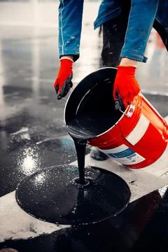 Close-up shot of a worker applying black epoxy resin from a bucket Stock-Fotos