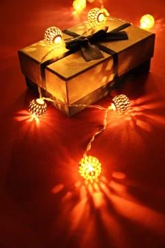 Close up shot of a wrapped gift under glowing Christmas lights on red backgro Stock Photos