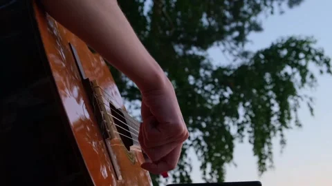 Close-up shot young woman's hands playing guitar on the seashore at sunset. Stockbeeldmateriaal 247230510