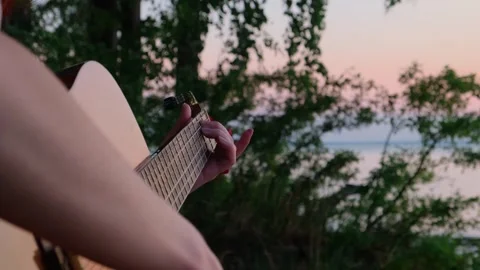 Close-up shot young woman's hands playing guitar on the seashore at sunset. Stock Footage 247491693