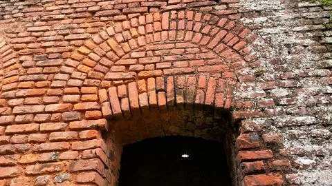 Close-up showcases a rustic orange brick archway, partially covered in lichen 스톡 사진