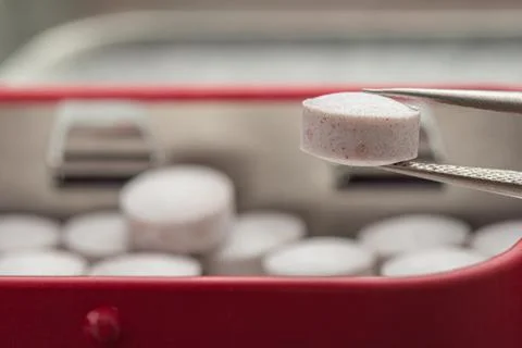 Close-up shows a single tablet held by tweezers Photos