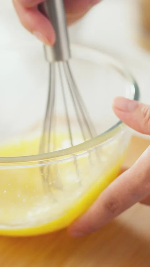 Close-up shows a womans hands gripping a whisk beating raw yellow eggs in a Stock Footage 338200387