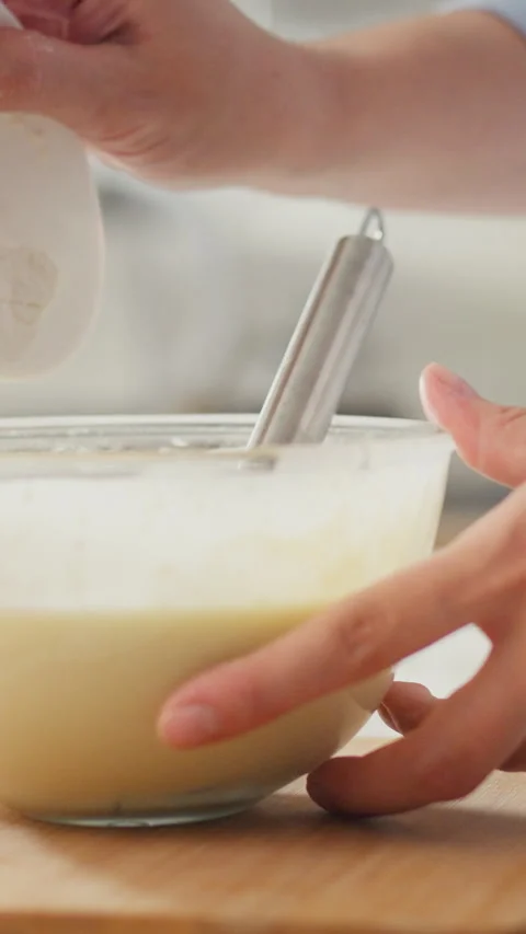 Close-up shows a womans hands gripping a metal whisk beating raw yellow eggs Stock Footage 338200437