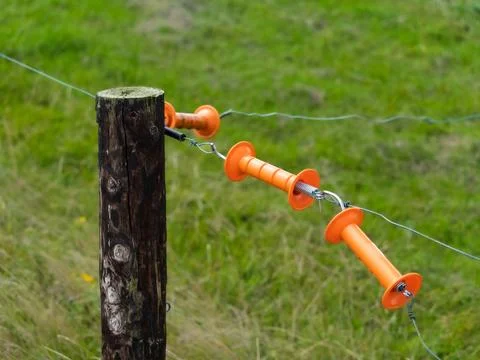 A close up shows a wooden fence post with orange electric insulators. Stock Photos