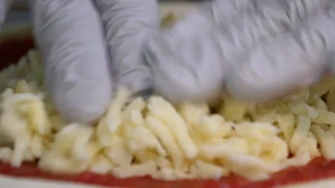 Close-up of Shredded Mozzarella Cheese Being Sprinkled onto Fresh Pizza Dough wi Stock Footage 337676891