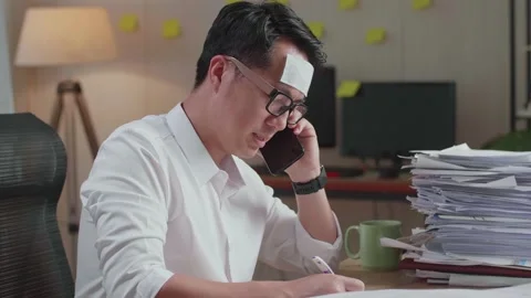 Close Up Of Sick Asian Man Talking On Phone And Taking Note While Working Stock Footage 196120441