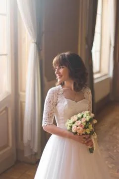 Close-up side portrait of the smiling bride looking through the castle window. Stock Photos