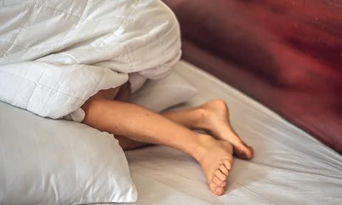 Close-up side view child boy leg knees feet stick out under white blanket on bed Stock Photos