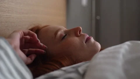 Close-up side view of of cute young woman waking up and opening eyes while lying 스톡 동영상 166465676