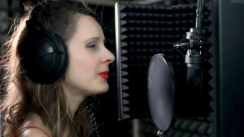 Close-up side view of female singer star talent in headphones singing into micro Video stock 119259816