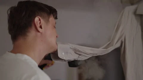Close-up side view of focused man steaming shirt using handheld garment steamer Stock Footage 318518438
