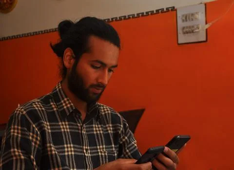 Close-up side view of a handsome bearded man with hair bun, holding two phones Stock Photos