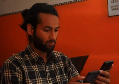 Close-up side view of a handsome bearded man with hair bun, holding two phones Stock Photos