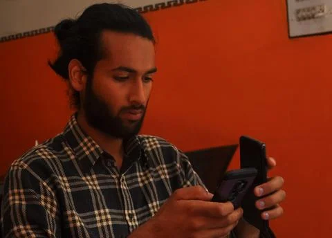 Close-up side view of a handsome bearded man with hair bun, holding two phones Stock Photos