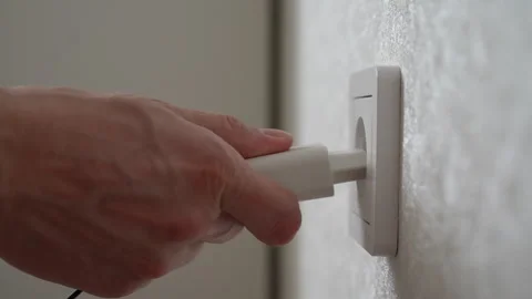 Close-up side view of male hand inserting white electrical plug into white wall Stock Footage 297953708