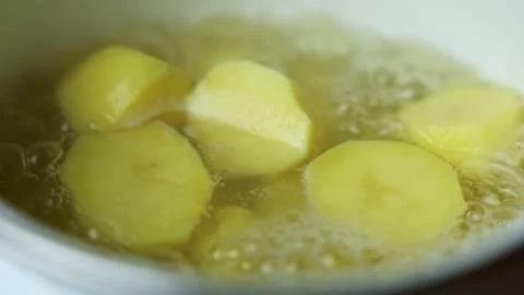 Close-up side view of peeled yellow potatoes boiling in water in a white Stock Footage 317141999