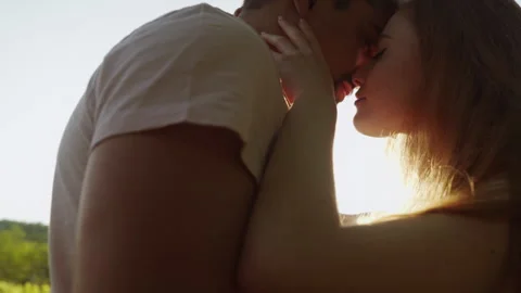 Close up side view portrait of a couple hugging and kissing against sunset Stock Footage 245182412