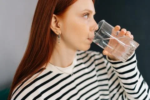 Close-up side view of thirsty redhead female holding glass, drinking still water Stock Photos
