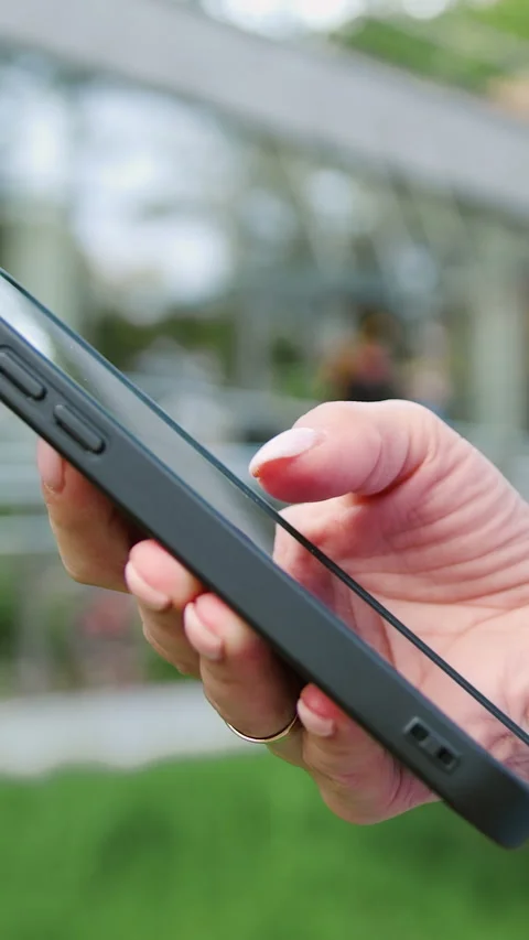 Close-up side view of a woman's hand holding and using a smartphone outdoors, sc Stock Footage 329377707
