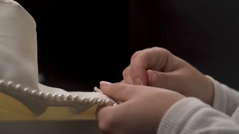 A close-up side view of woman's hands sewing beaded lace down the wedding dress Video stock 99047995