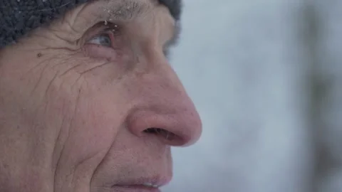 Close side view of wrinkled face of old man stands outdoor in snowy blizzard. Video stock 146320923