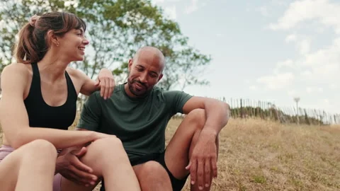 Close up side view of young athletic couple relaxing in the park, sitting on the Stock Footage 295563707