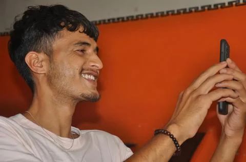 Close-up side view of a young guy smiling while using his phone while sitting  Stock Photos