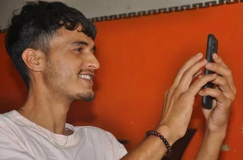Close-up side view of a young guy smiling while using his phone while sitting  Stock Photos
