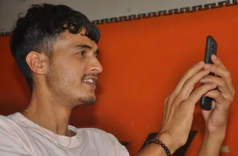 Close-up side view of a young guy smiling while using his phone while sitting  Stock Photos