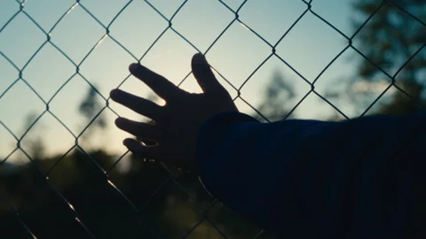 Close-up of a silhouette hand passing over the chain link fence at sunset Stock Footage 276164479