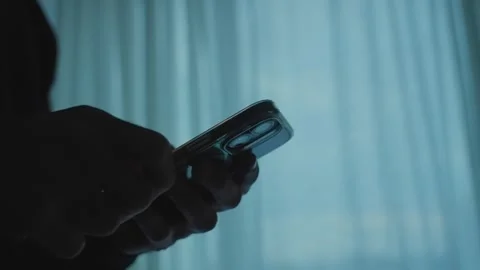 Close up silhouette of a person's hands holding a mobile phone and scrolling Stock Footage 341072703