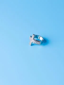 Close-up of a silver cross-shaped ring with white rhinestones against a blue  Stock Photos