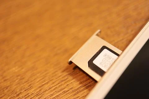 Close up of a SIM Card inserted into a smartphone tray slot on a wooden tab.. Stock Photos