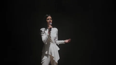 Close-up of a singer in a white suit singing on stage on a black background. Stockbeeldmateriaal 125317899