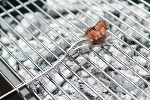 Close-up of a single piece of bacon on a fork over hot charcoal grill grate Stock Photos