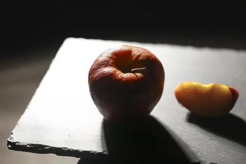 Close-up of a single red apple casting a long shadow across a slate board Stock Photos