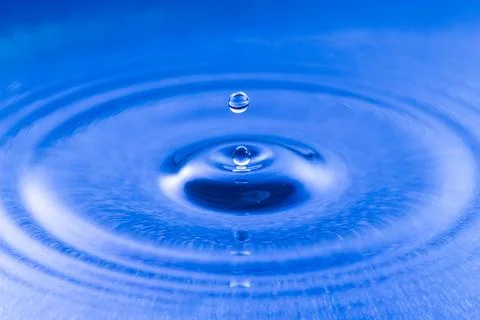 Close-up of a single water drop falling into blue liquid creating ripples Stock Photos