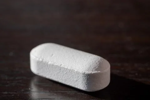 Close-up of a single white tablet pill placed on a dark wooden surface Foto stock