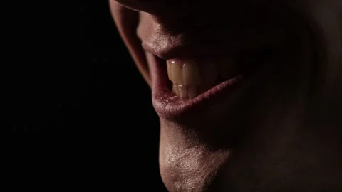 Close-up of a sinister smile in dramatic low lighting, showing slightly parted Stock Footage 305582027