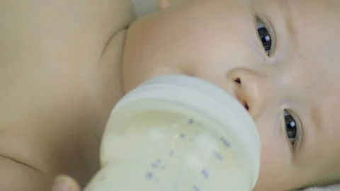 Close-up of a six months old boy lies on a bed and eats milk from a bottle. Stock Footage 99724099