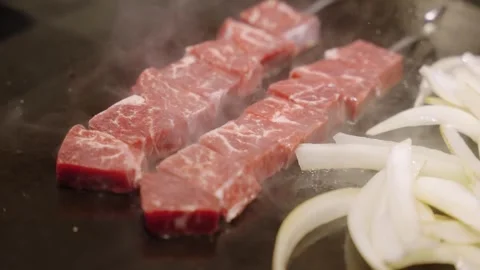 Close-up of Sizzling Wagyu Beef Cubes and Sliced Onions on a Japanese Teppanyaki Stock Footage 337441021